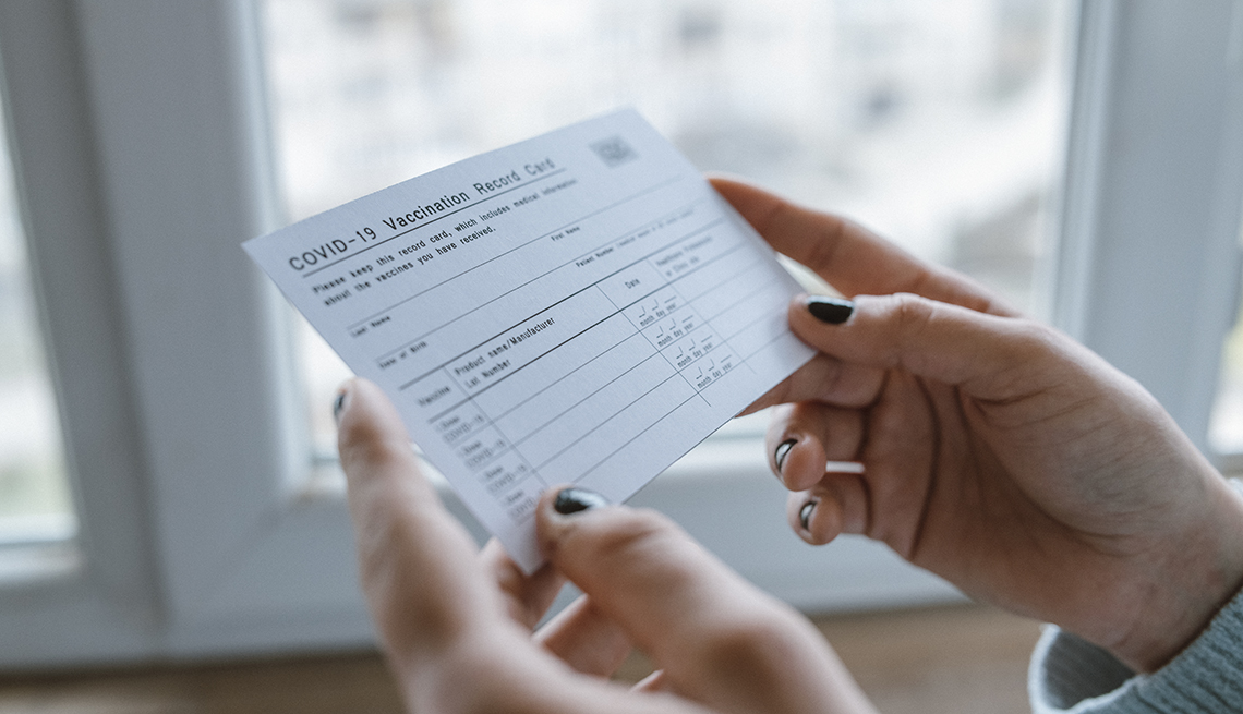 Close up of cropped female hands holding COVID-19 vaccination record card.
