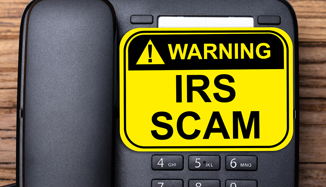 desktop phone with a big yellow warning sticker that says IRS Scam