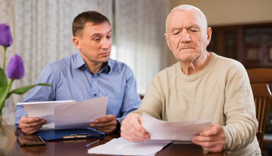 Adult man with his elderly father looking worriedly at papers analyzing their finances at home Adult man with his elderly father looking worriedly at papers analyzing their finances at home