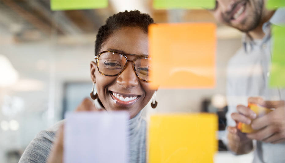 A smiling woman brainstorming with sticky notes on a glass wall