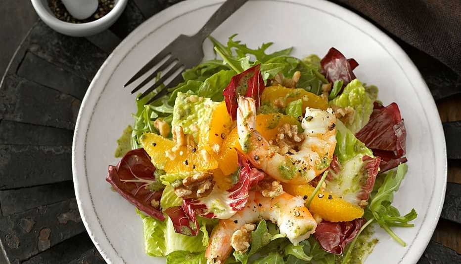 A close-up view of orange and black pepper shrimp salad on a plate