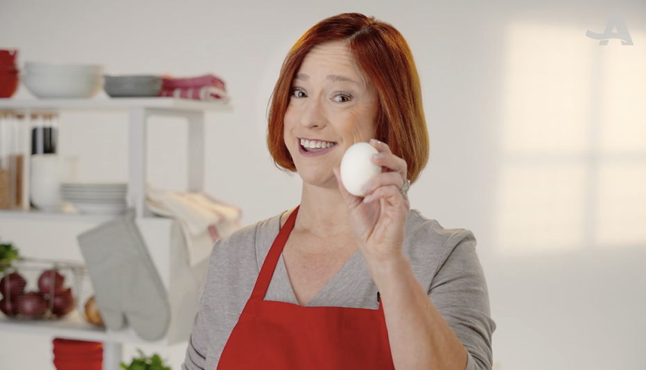 A woman smiling and holding up an egg in her hand
