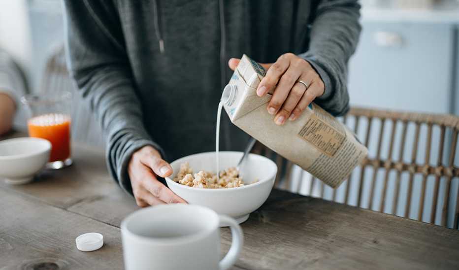 A person pouring milk into a cereal bowl