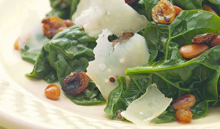 A close-up view of sautéed spinach with pine nuts and raisins on a plate