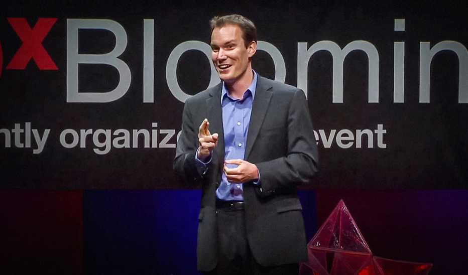 A man, Shawn Achor, speaking on stage at a TED event