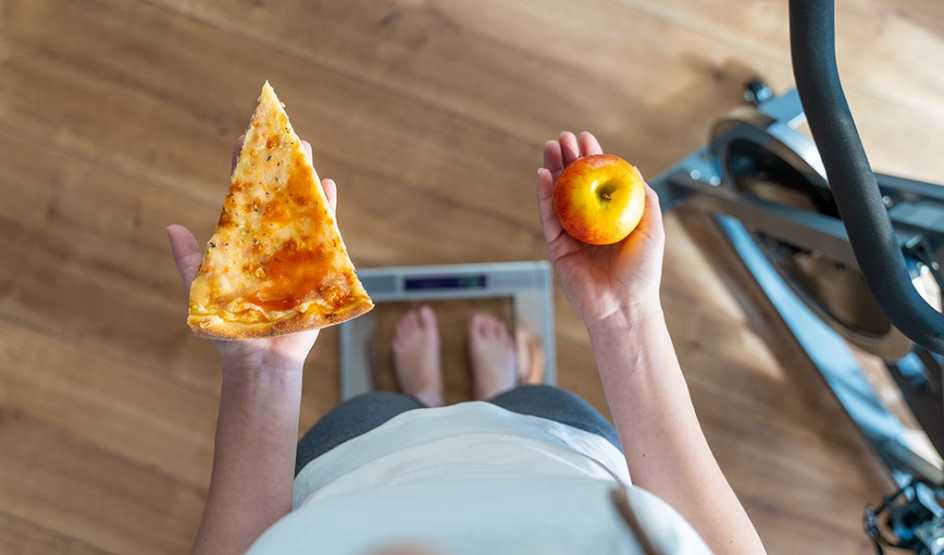 An overhead view of a person holding a slice of pizza in one hand an apple in another
