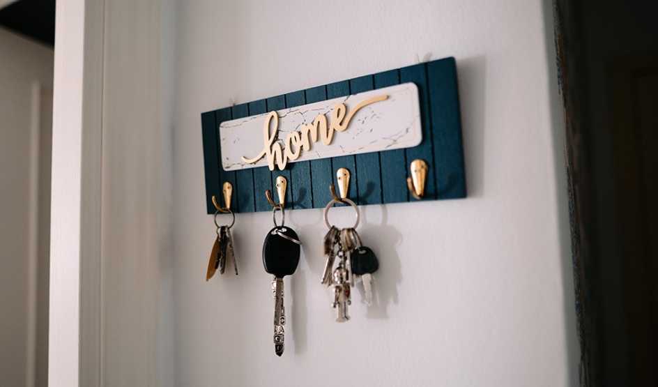 A wooden key rack on the wall with three sets of keys hanging from it