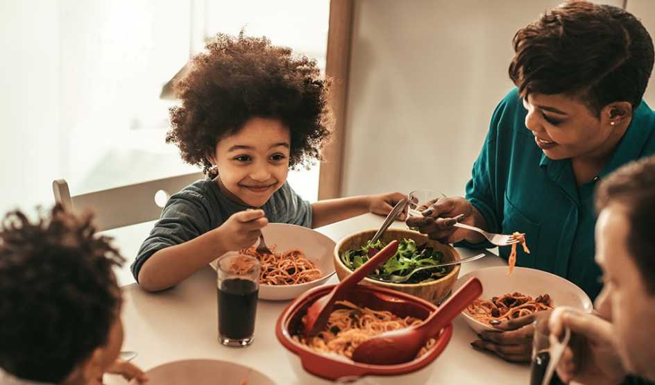 A young child is smiling as they eat lunch at a table with their family