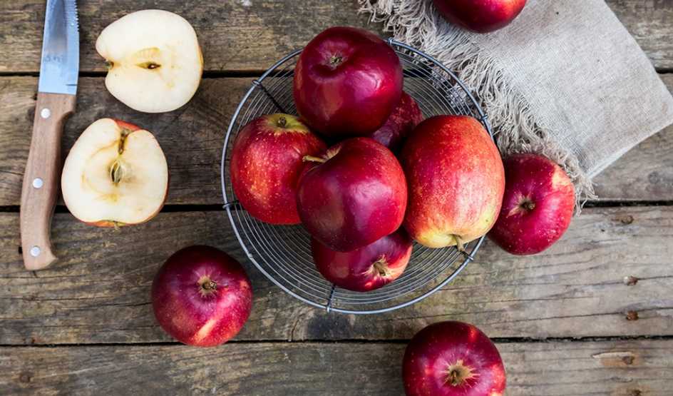 A close-up view of a bowl of apples on dark wood